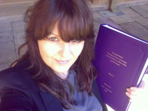 Me with long brunette hair holding up the bound copy of my PhD