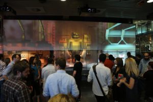 Photo of people in front of large screens with robot